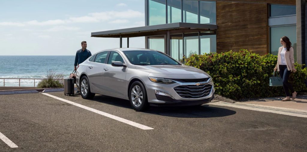 A silver 2022 Chevrolet Malibu parked in a parking spot and a man and a woman are walking back to their car to get in.