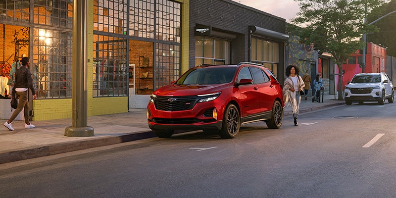 A red 2024 Chevy Equinox parked on a busy shopping street.