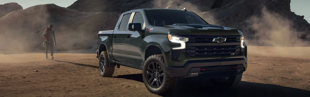 A Chevrolet Silverado 1500 ZR2 pickup truck driving through a dusty desert terrain, with a person walking in the background.