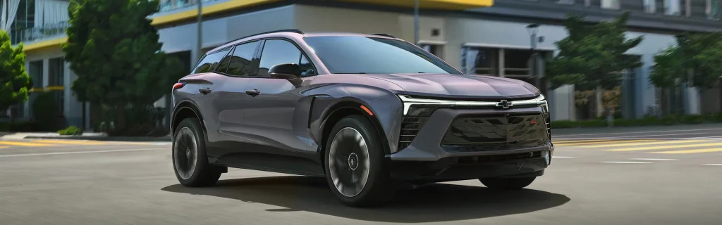 Chevrolet electric SUV driving through a city street in a modern urban setting, shown in front three-quarter view.