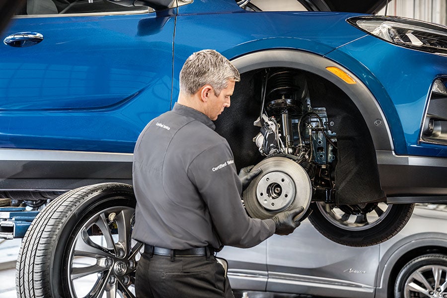 Technician inspecting the brake assembly on a blue SUV.